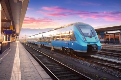 Beautiful view with modern high speed train on the railway station and colorful sky with clouds at sunset in Europe. Industrial landscape with blue train on railway platform. Railroad background